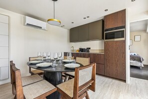 A modern kitchen with a built-in oven and microwave, a dining area with a round table and chairs, and a visible air conditioning unit. - Lavie Maison | Le Marais & Rivoli (Paris)