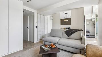 A modern living room with a grey sofa, a coffee table with pastries, and a kitchen area in the background.