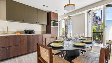 A modern kitchen with dark wooden cabinets, a round dining table set for six, and a view of a historic building through large windows.