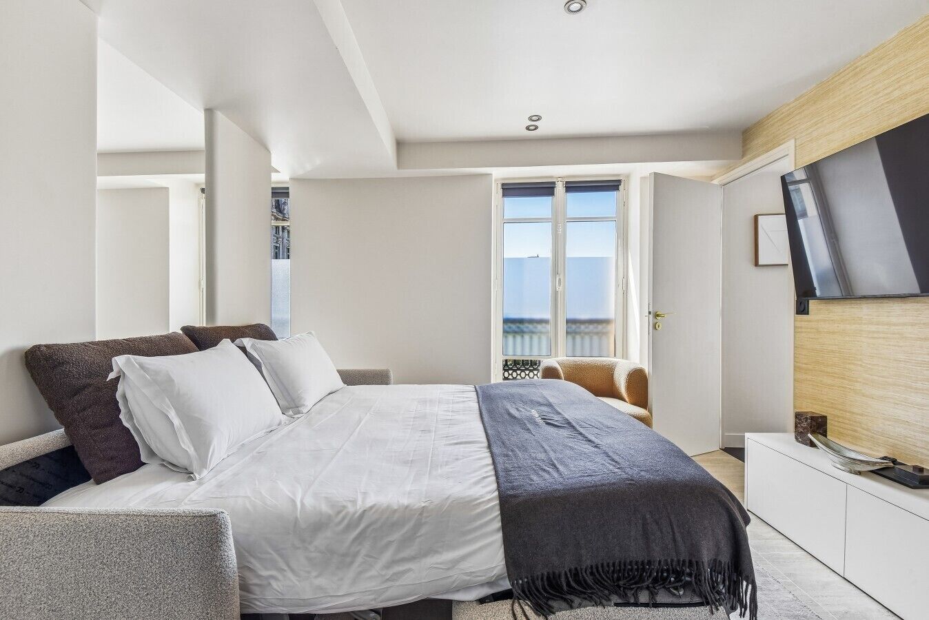 A modern hotel room with a bed, a television on the wall, and a view of the outside.