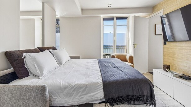 Moderni hotellihuone, jossa on sänky, seinälle asennettu televisio ja näkymä ulos.