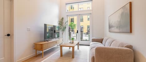 A modern living room with a sofa, TV, wooden console, and a large window.