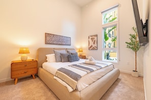 Un dormitorio con cama, lámparas de noche, mesita de noche, ventana con vistas y una planta en maceta.