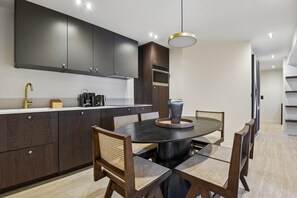 A modern kitchen with dark cabinetry, a round dining table, and a pendant light. - Lavie Maison | Rivoli & Louvre (Paris)