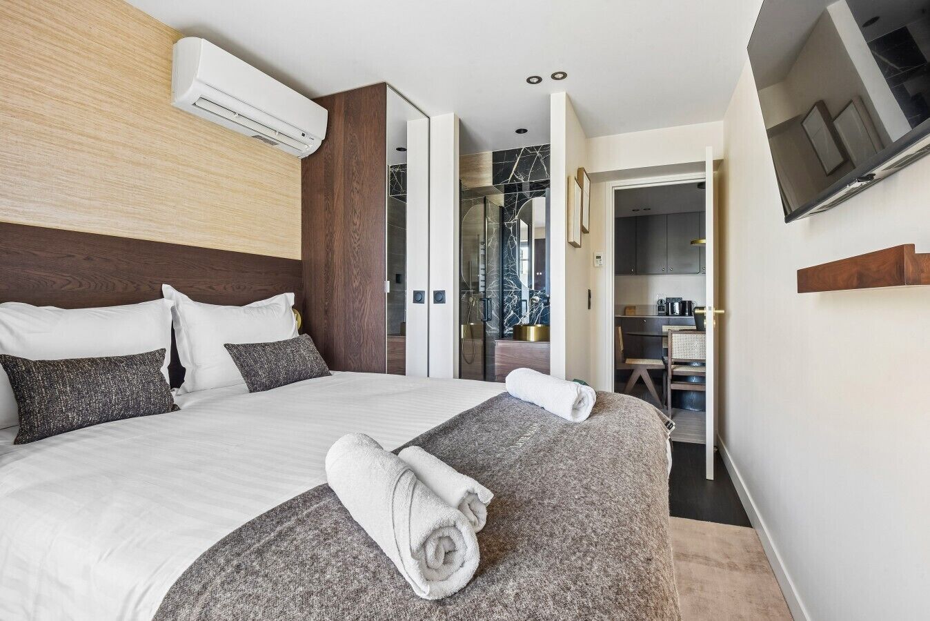 A modern hotel room with a large bed, a flat-screen TV mounted on the wall, and a separate dining area.