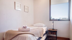 Ein Schlafzimmer mit einem Bett, einem Nachttisch mit Lampe, einem Fenster mit Ausblick und zwei gerahmten Bildern an der Wand.