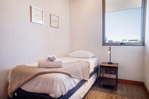 A bedroom with a bed, a bedside table with a lamp, a window with a view, and two framed pictures on the wall. - Cozy Getaway Oasis 2BR in Las Condes (Las Condes)