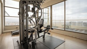Ein Fitnessstudio mit großem Fenster, einem Krafttrainingsgerät und Blick auf eine Stadtlandschaft.