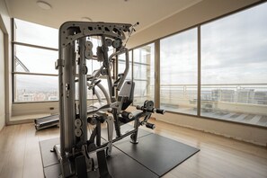 A gym with a large window, a weight machine, and a view of a cityscape. - Cozy Getaway Oasis 2BR in Las Condes (Las Condes)