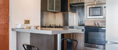 A modern kitchen with a central island, stainless steel appliances, and black bar stools.