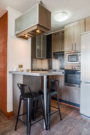 A modern kitchen with a central island, stainless steel appliances, and black bar stools. - Cozy Getaway Oasis 2BR in Las Condes (Las Condes)
