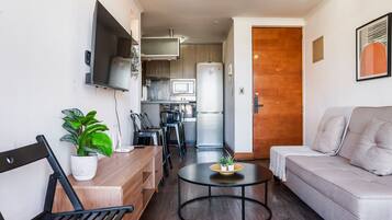 Un espacio habitable compacto con kitchenette, un sofá, una mesa de comedor y un televisor montado en la pared.