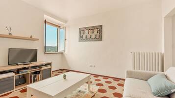 A modern living room with a flat-screen TV, a sofa, a coffee table, and a window with a view.