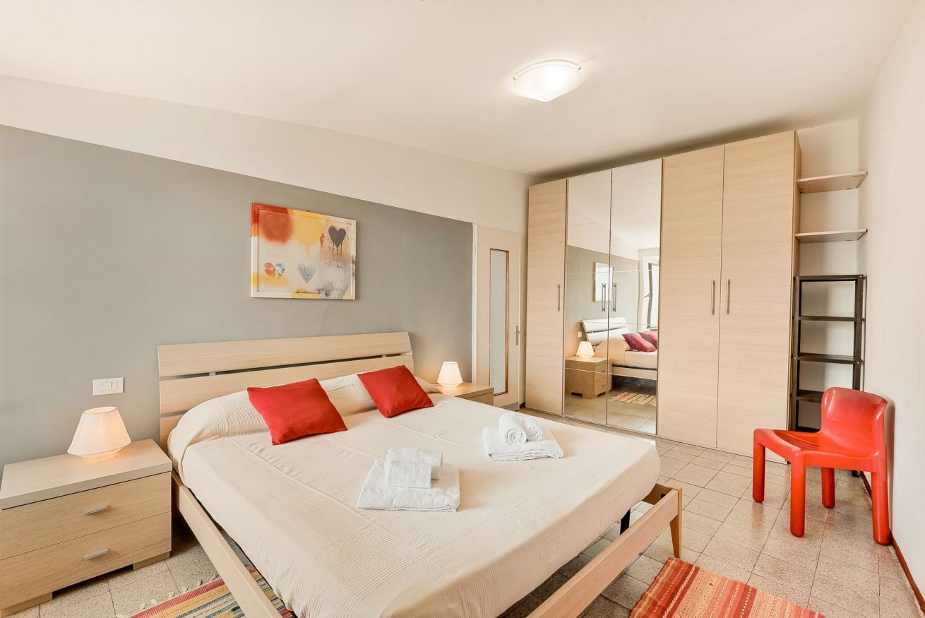 A modern bedroom with a large bed, bedside tables, a wardrobe, and a mirror.