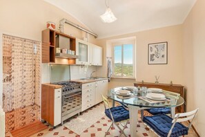A compact kitchen with a gas stove, oven, and white cabinets. There's a dining table with chairs and a view of the outdoors through a window. - [SanVenerio] Sea view 5 TERRE (La Spezia)