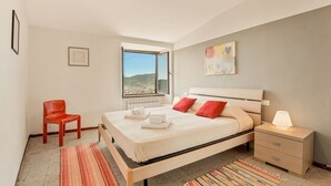Une chambre à coucher avec un lit, une table de chevet, une chaise, une fenêtre donnant sur un paysage agréable et un tableau accroché au mur.