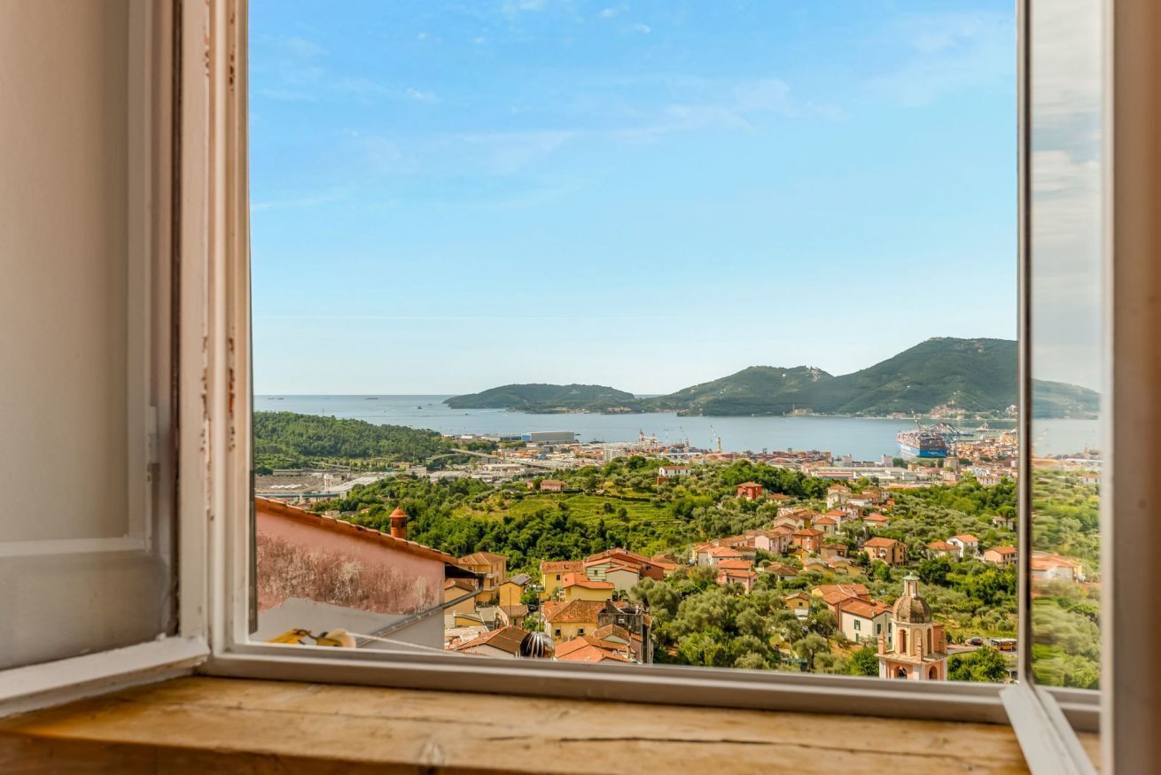 A coastal town view from a window, with buildings, greenery, and a body of water in the distance.