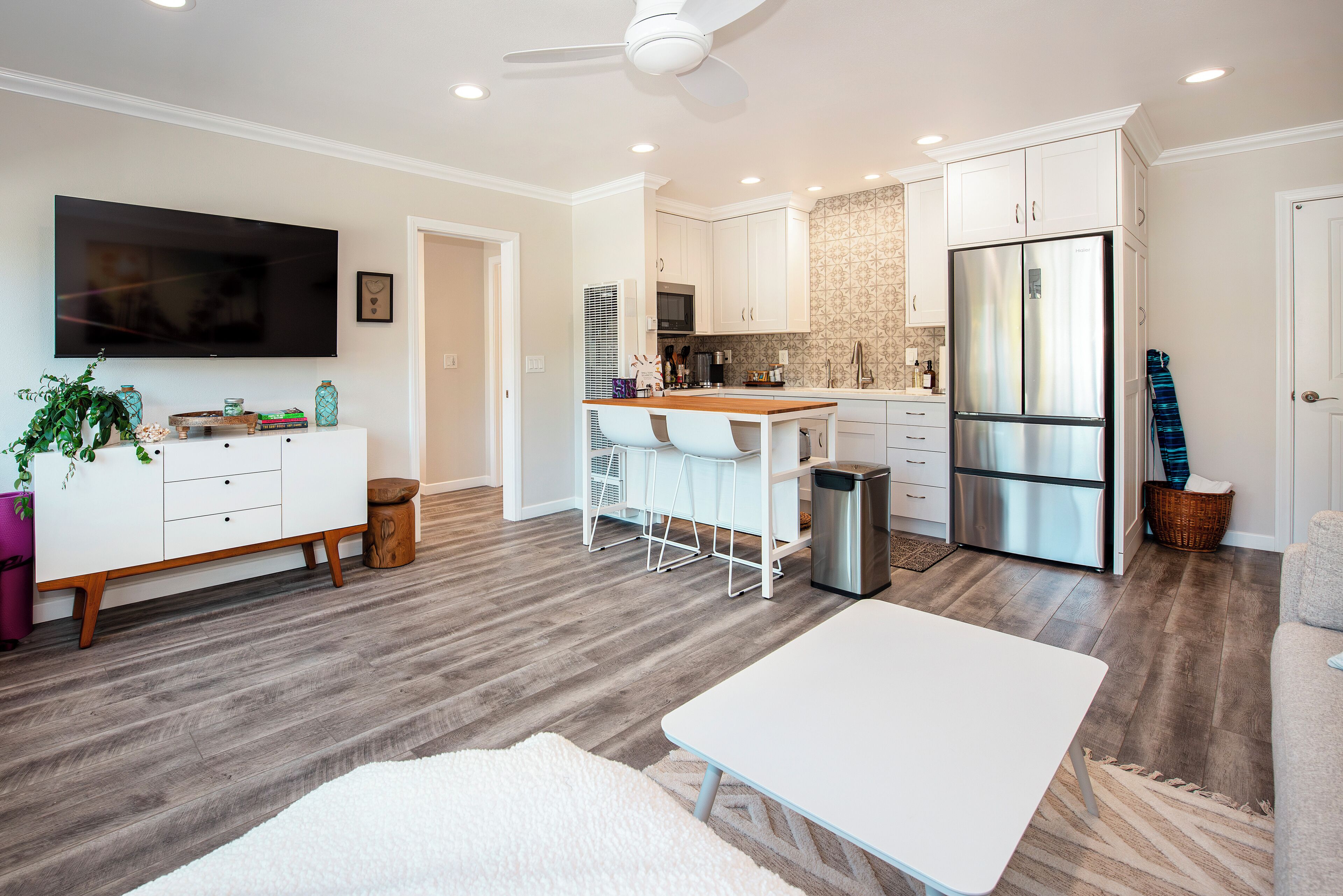 A modern kitchen with white cabinets, a stainless steel refrigerator, and a dining area with a white table and chairs.