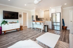 A modern kitchen with white cabinets, a stainless steel refrigerator, and a dining area with a white table and chairs. - Lux Coastal Retreat • Steps to Sand• Heated Pool by Maera (Carpinteria)
