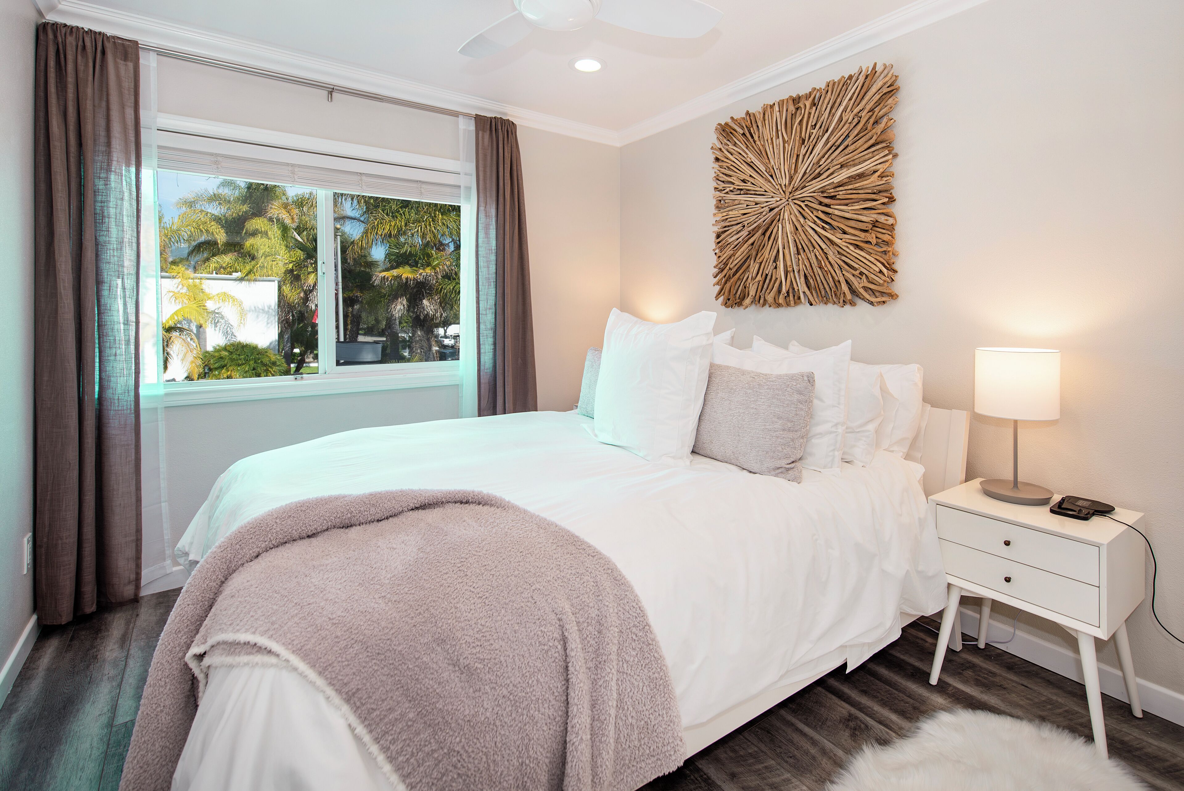 A bedroom with a bed, a nightstand, a lamp, a window with curtains, and a wall decoration.