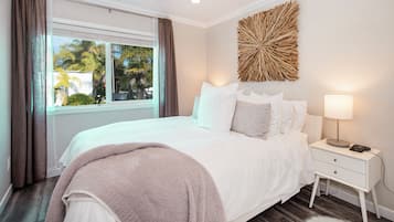 A bedroom with a bed, a nightstand, a lamp, a window with curtains, and a wall decoration.