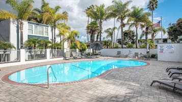 A swimming pool with a tiled deck, lounge chairs, and palm trees.