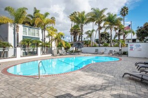 A swimming pool with a tiled deck, lounge chairs, and palm trees.