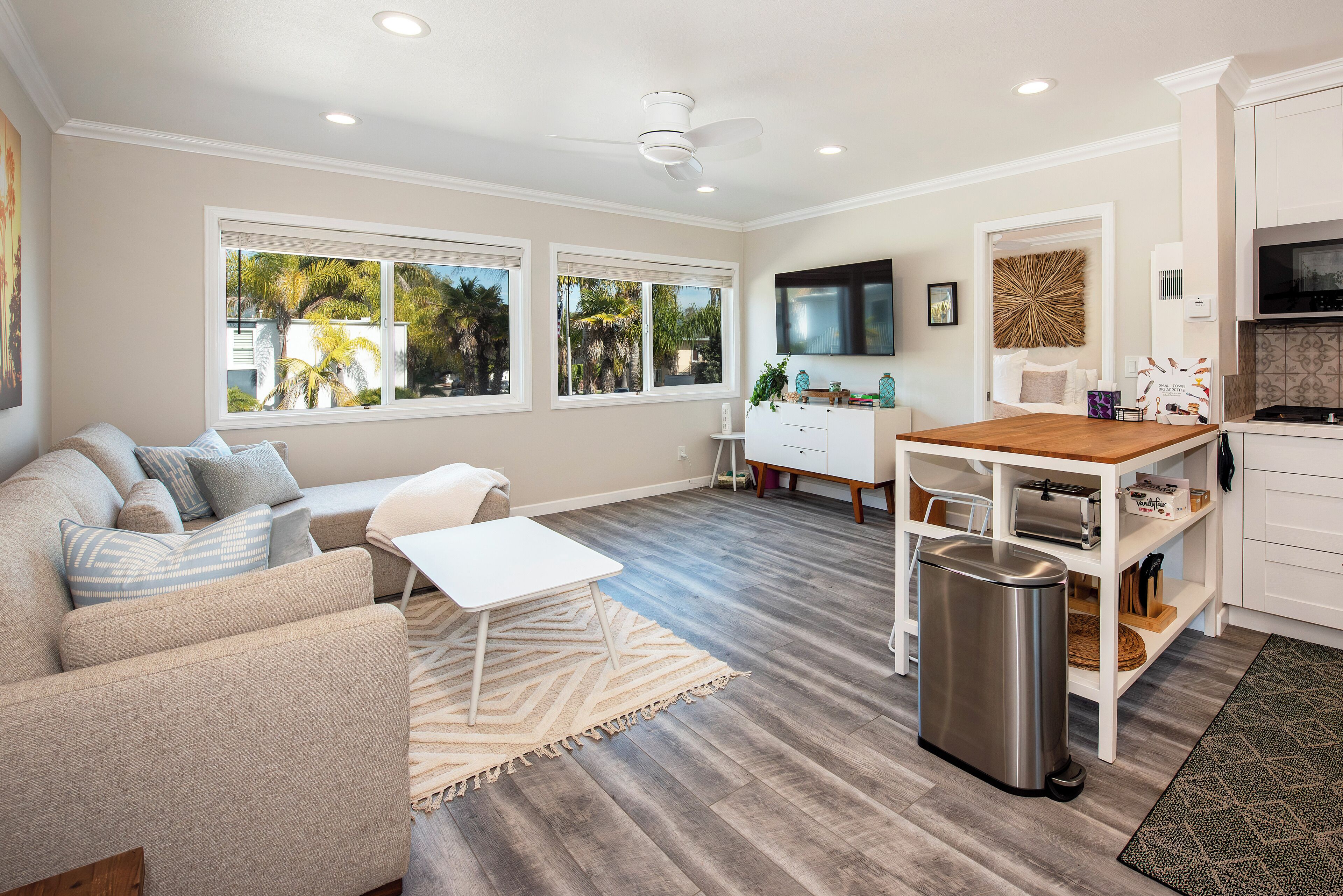 A modern living room with a sofa, a coffee table, and a TV. There is a kitchen area with a microwave and a toaster.