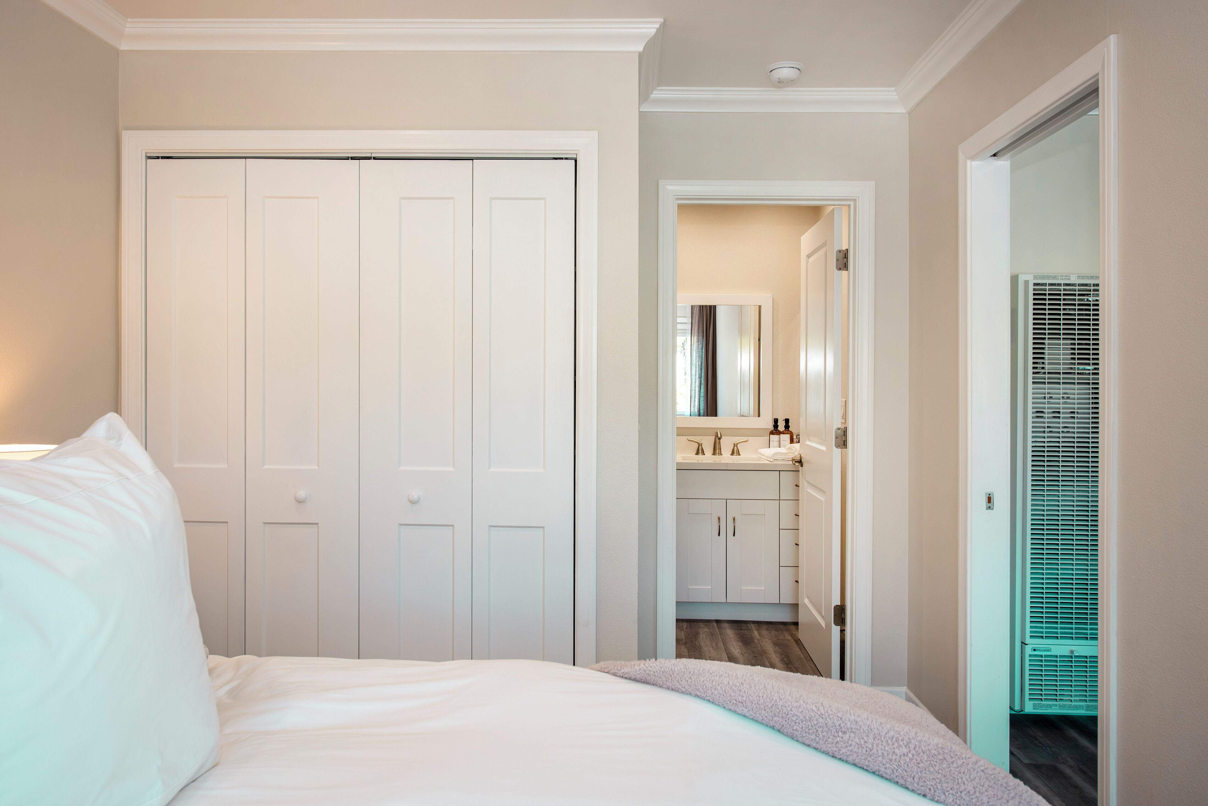 A hotel room with a bed, a bathroom with a sink and mirror, and a hallway leading to another room.