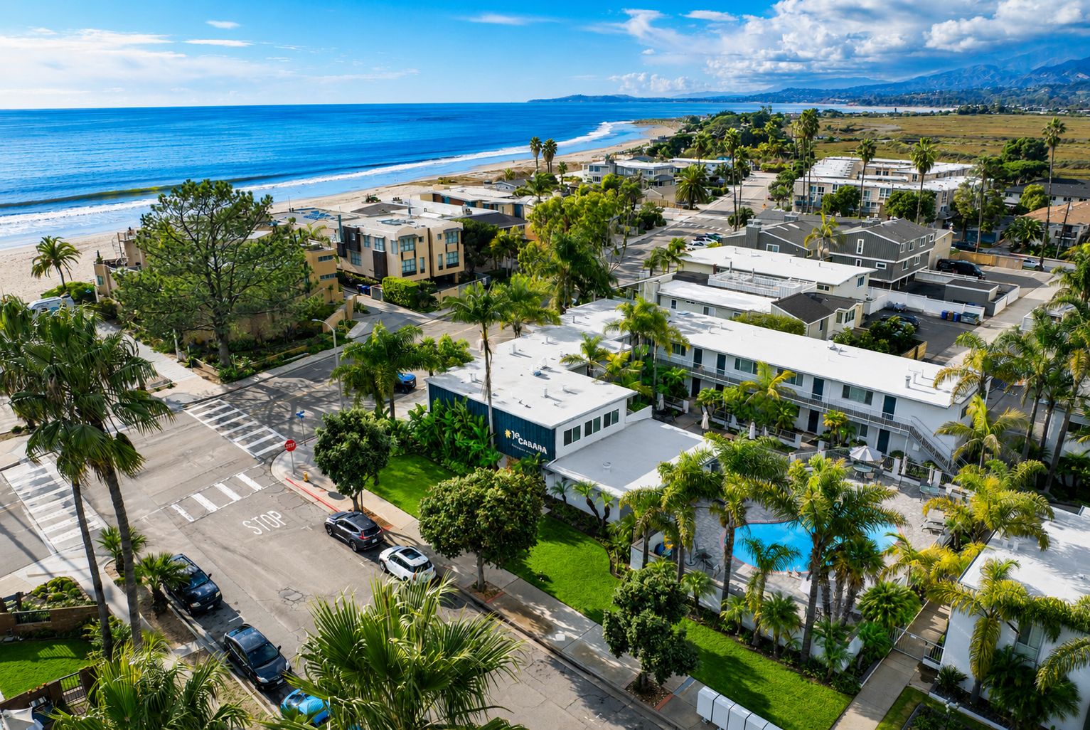 A coastal residential area with modern buildings, a visible swimming pool, and a clear view of the beach.