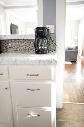 A kitchen with a coffee maker on the counter, a tiled backsplash, and a wooden floor.
