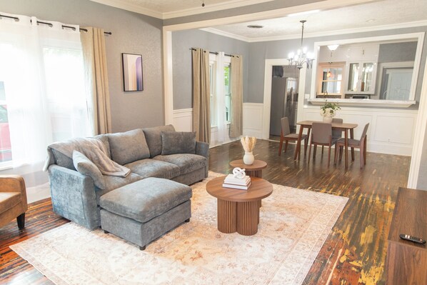 A living room with a grey sectional sofa, a coffee table, and a dining area with a table and chairs.