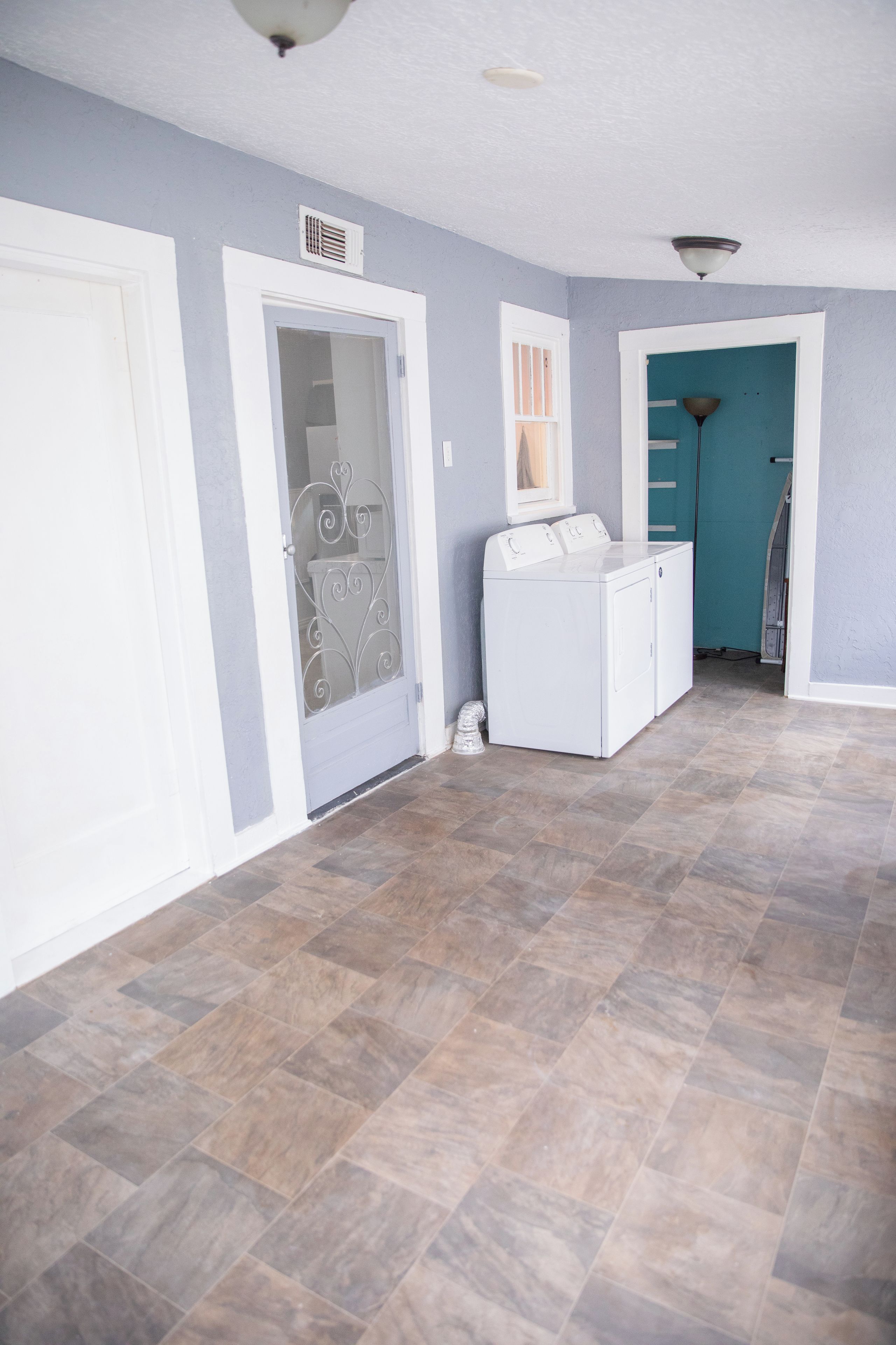 Un lavadero con lavadora y secadora, una puerta con un panel de vidrio decorativo, y un pasillo con piso de baldosas.