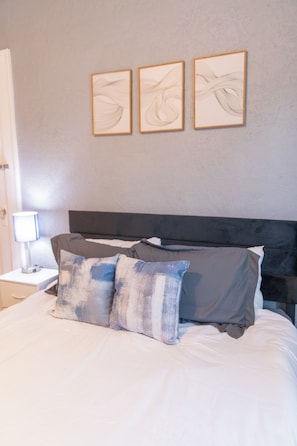 A neatly made bed with two pillows and a dark headboard. There are three framed artworks on the wall above the bed.