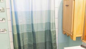 Et badeværelse med badeforhæng, toilet, håndvask og skab.