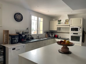 A modern kitchen with white cabinetry, a large window, and a clock on the wall.