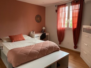 A bedroom with a bed, a desk, a chair, a dresser, and a window with curtains.