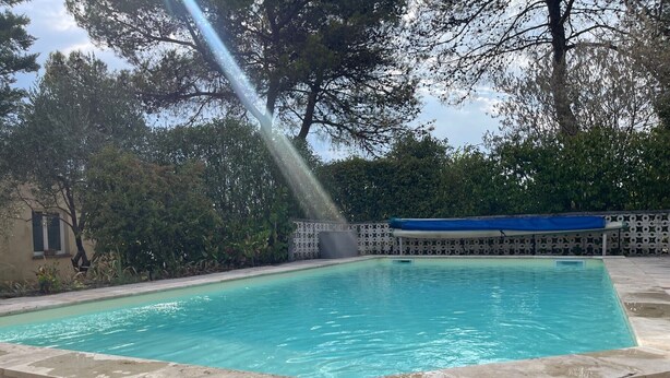 A rectangular swimming pool with a clear blue water surface, surrounded by a stone deck and a decorative fence.