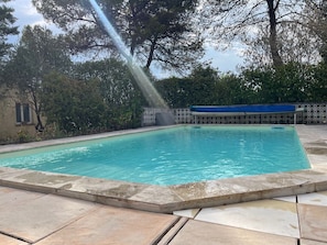 Ein rechteckiger Swimmingpool mit glasklar blauem Wasser, umgeben von einer Steindeck und einem dekorativen Zaun.
