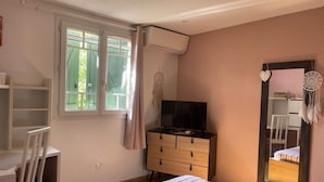 A bedroom with a bed, a TV on a dresser, a wardrobe, a desk, and a window with curtains.