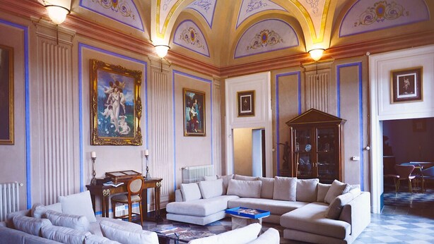 A spacious living room with a large sectional sofa, a coffee table, and a fireplace. There are framed pictures on the walls and a chandelier hanging from the ceiling.