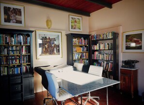 Une salle de bibliothèque avec une grande table, des étagères et des tableaux encadrés aux murs.
