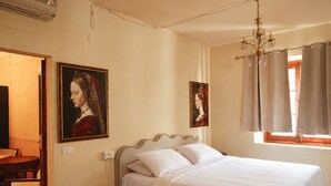 A bedroom with a bed, a nightstand, a wooden table, and two paintings on the wall.