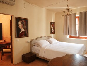 A bedroom with a bed, a nightstand, a wooden table, and two paintings on the wall.