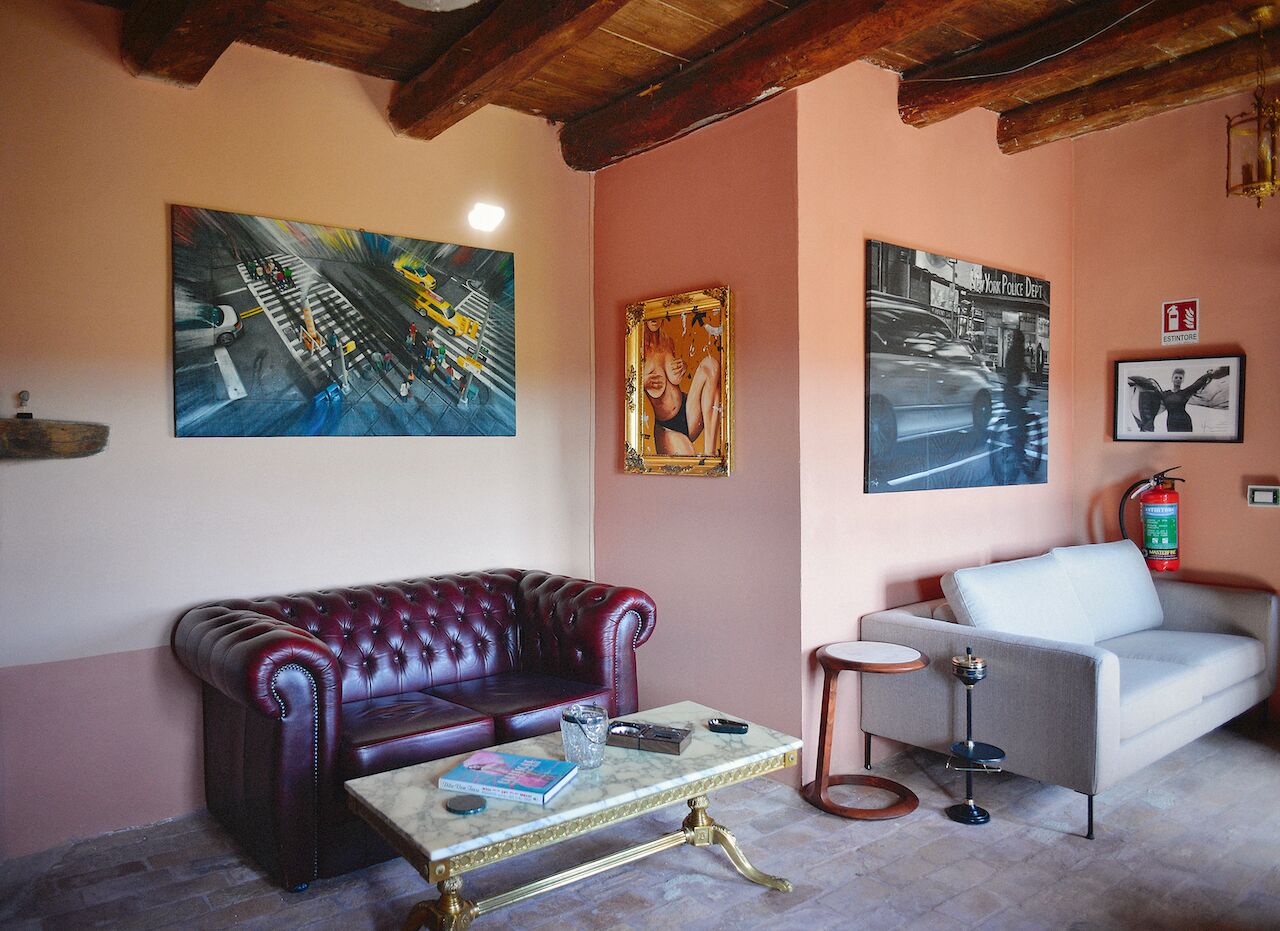 Un salon avec un canapé en cuir rouge, un canapé blanc et une table basse en marbre. Des tableaux ornent les murs et un extincteur est fixé au mur.