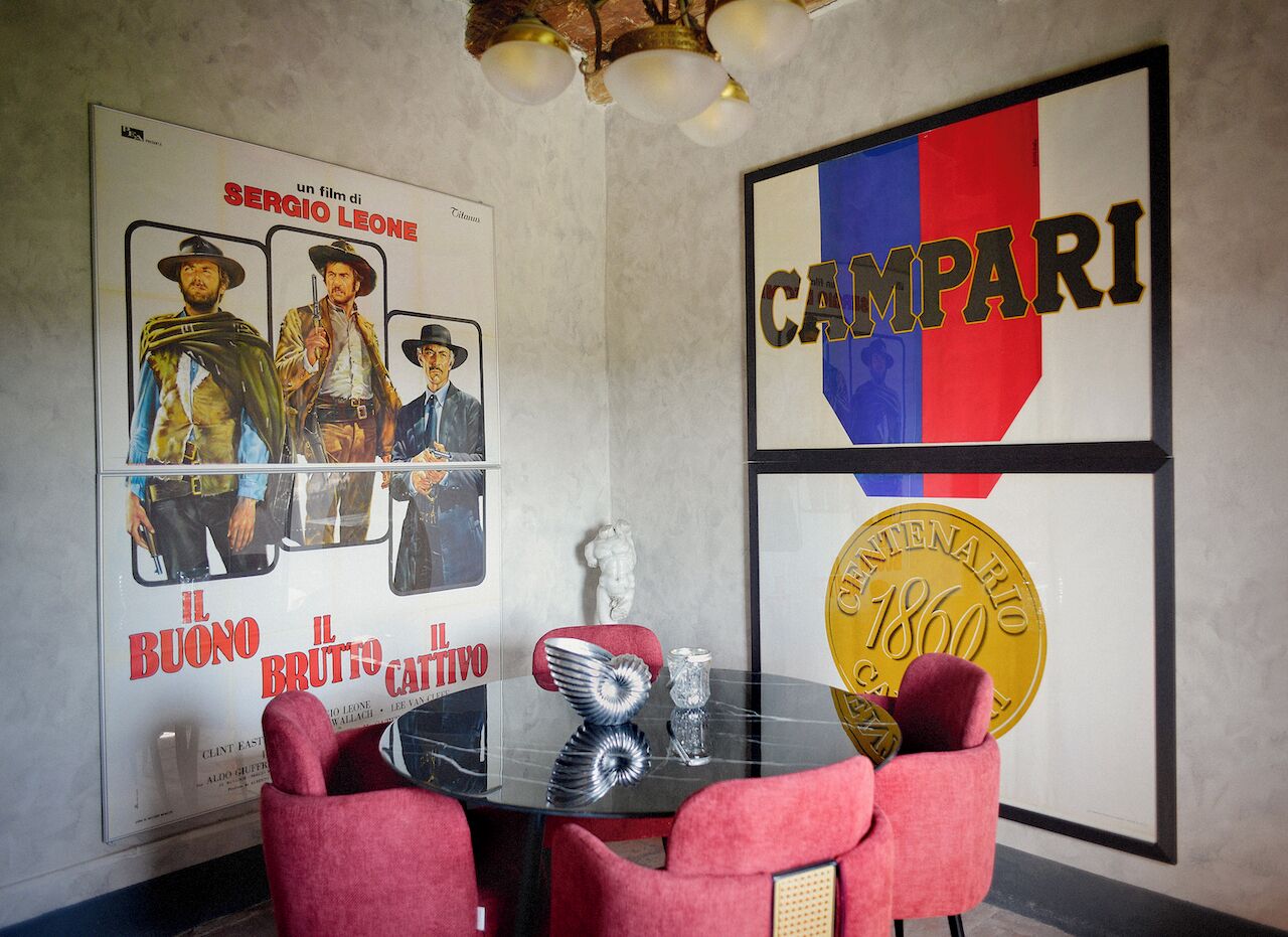 A room with a glass table, red upholstered chairs, a framed movie poster, and a wall with a flag and a historical coin.