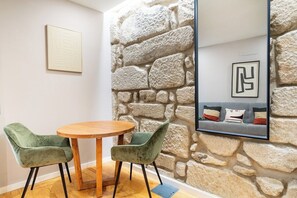 Ein Zimmer mit einer Steinwand, einem runden Holztisch, zwei grünen Stühlen und einem gerahmten Bild an der Wand.