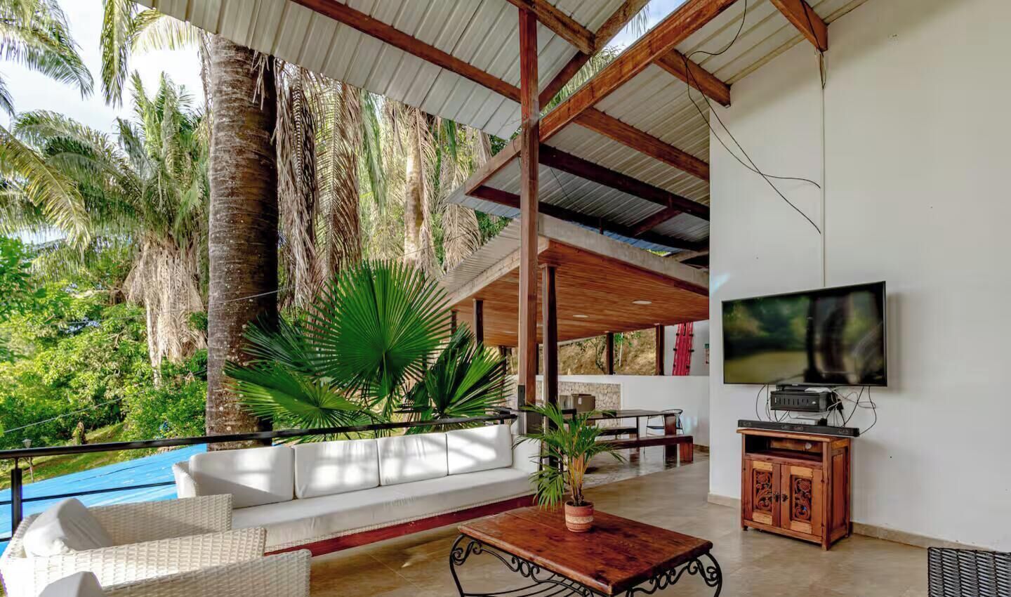 A spacious living area with a sofa, coffee table, and TV, overlooking a pool and lush greenery.