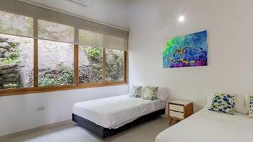Quarto com duas camas, uma janela com vista para o verde e um quadro na parede.