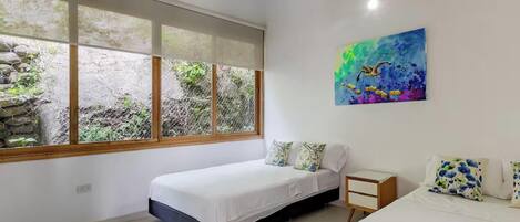 A bedroom with two beds, a window with a view of greenery, and a painting on the wall.